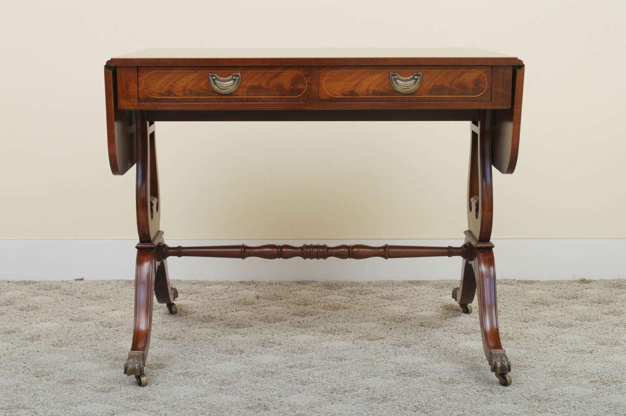 A beautiful Regency style inlaid, flame mahogany Sofa Table. The drop leaf top is above two drawers with two false drawers behind.  The table is raised on lovely lyre supports connected by a turned stretcher that leads to cast brass lion's paw feet